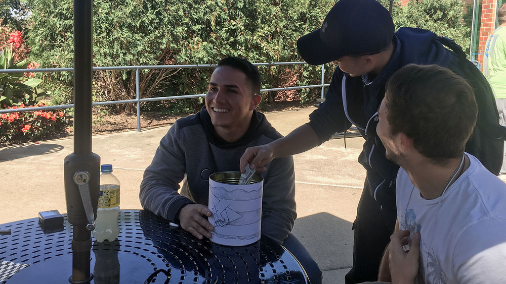 Students Pedro Escobar and Marcos Lopez collect a donation from Dash Phuyel in a can wrapped in a drawing of the Puerto Rican flag outside of Café Metro.