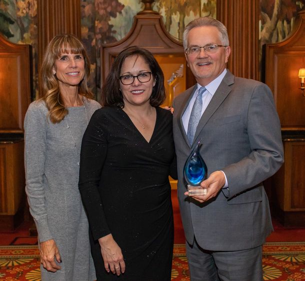 three people smiling at camera, one is holding a tear drop award 