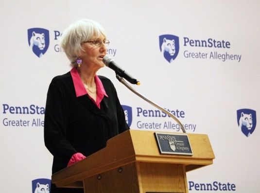 Woman speaking into a microphone that is attached to a wooden podium.