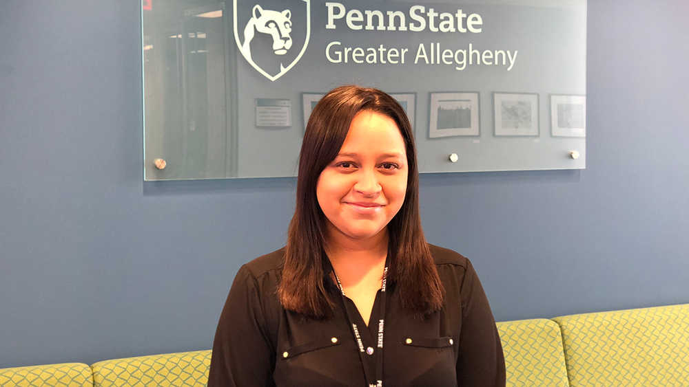 Ashley smiling and standing in front of the Greater Allegheny logo