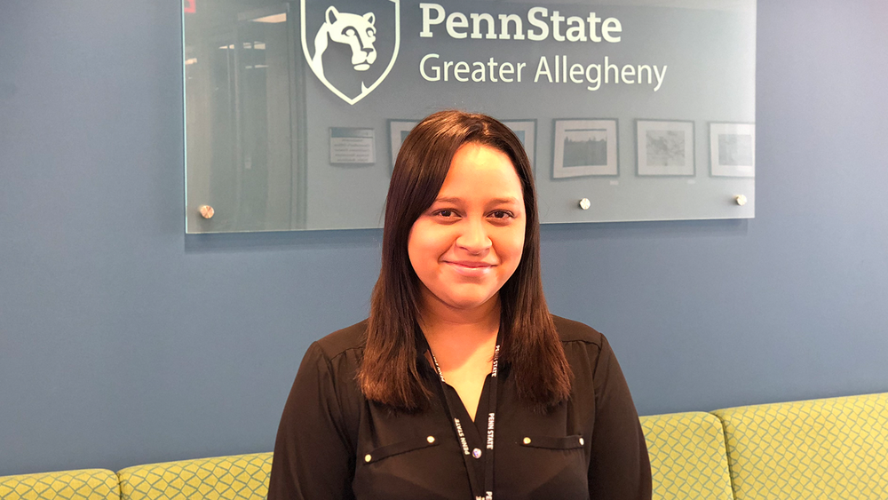 Ashley smiling and standing in front of the Greater Allegheny logo 