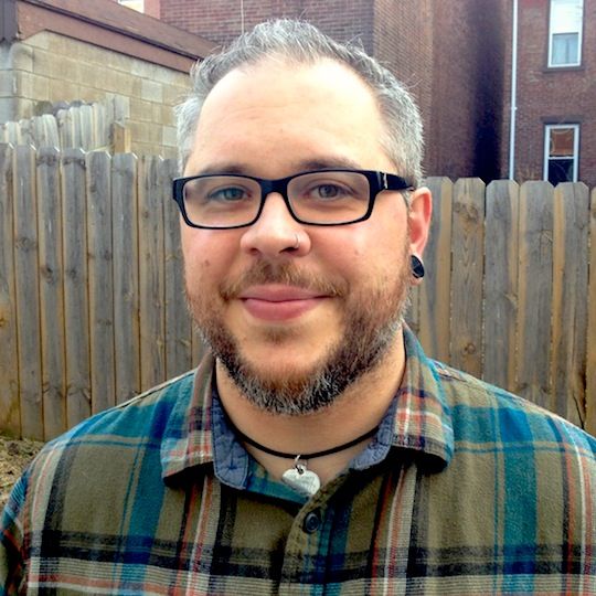 man smiling in front of wooden fence