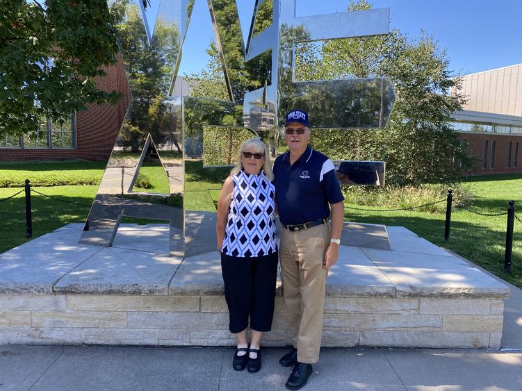 A couple standing in front of the WE ARE statue at University Park