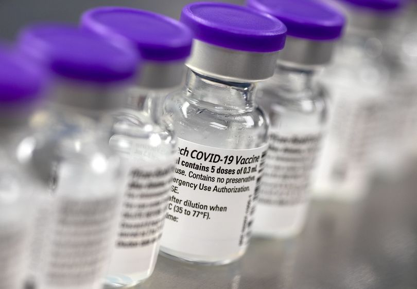 A row of vials show labels indicating they contain the COVID-19 vaccine.
