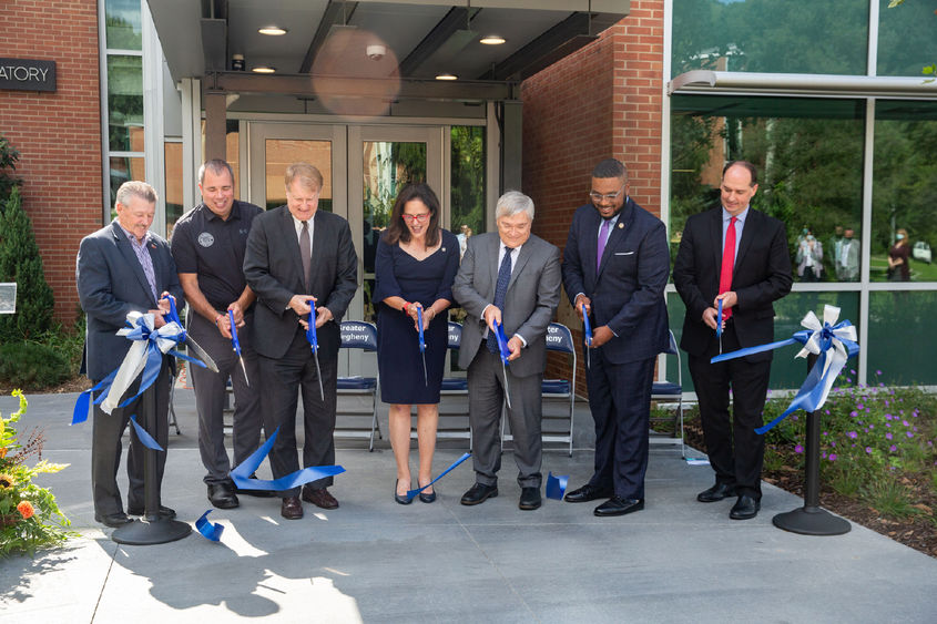 Group of people holding oversized scissors cut ribbon. 