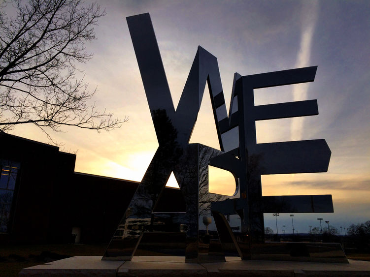 We Are sculpture silhouetted by the setting sun on Penn State University Park campus