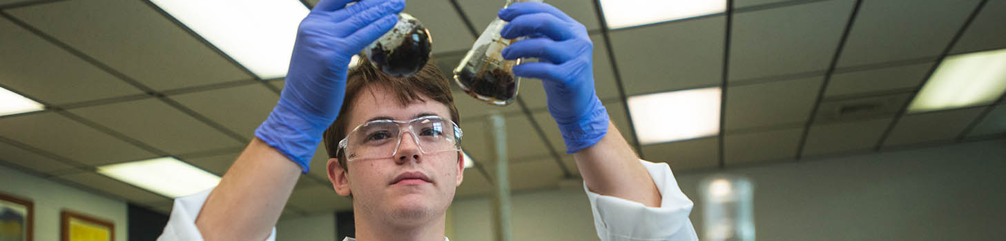 student holding beaker with safety glasses and gloves on